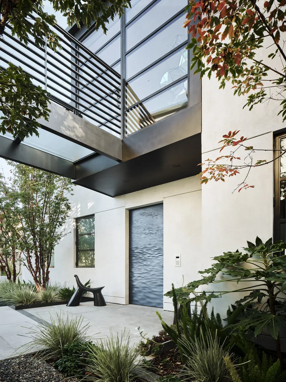 The entry under the steel stair — paperbark maple and grasses either side of the door, ferns in the shade