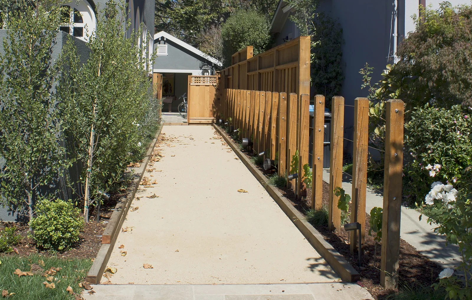 The side court, which doubles as a bocce court — decomposed granite running between the house and a post-and-wire grape trellis to a gate at the far end