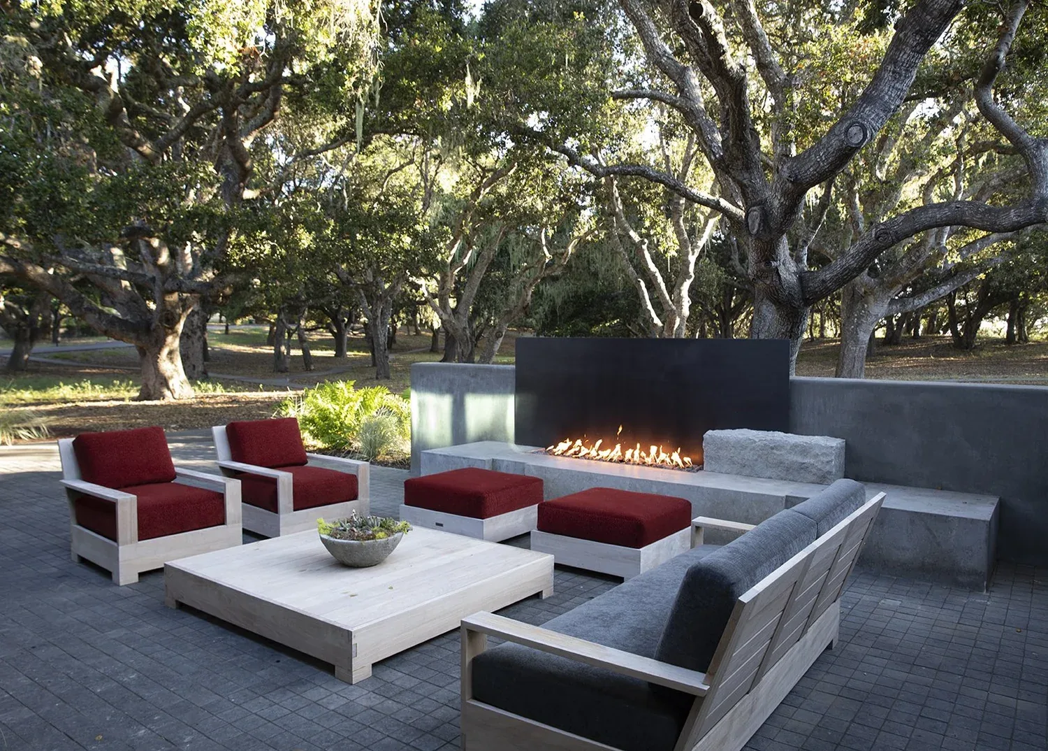 Carmel Contemporary Hacienda — the fire feature on the patio in the oak grove: a broad limestone base, a corten panel, dark stucco behind, lounge seating in front