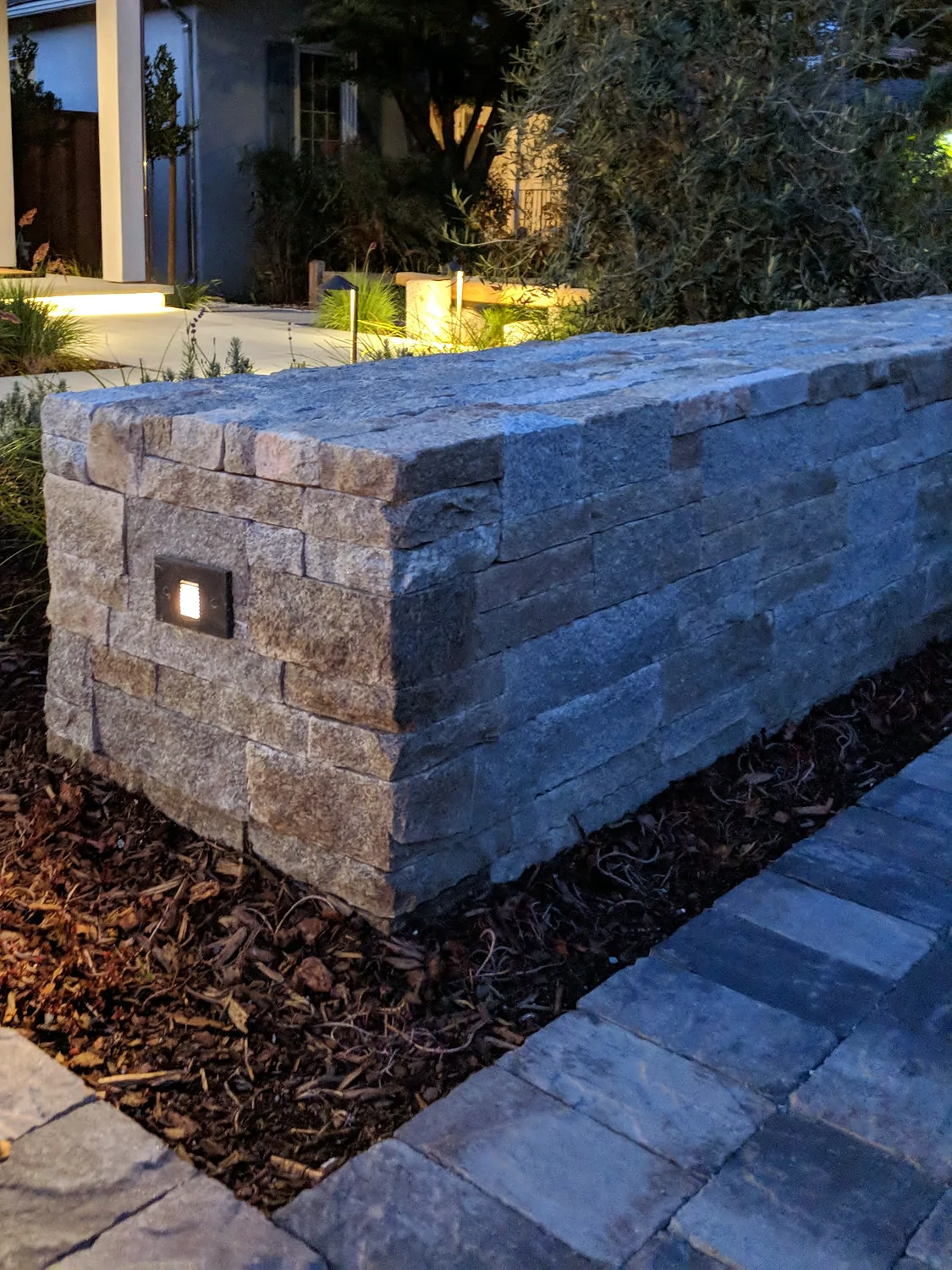 The low stone wall at the arrival, a step light set into its face, the lit entry beyond