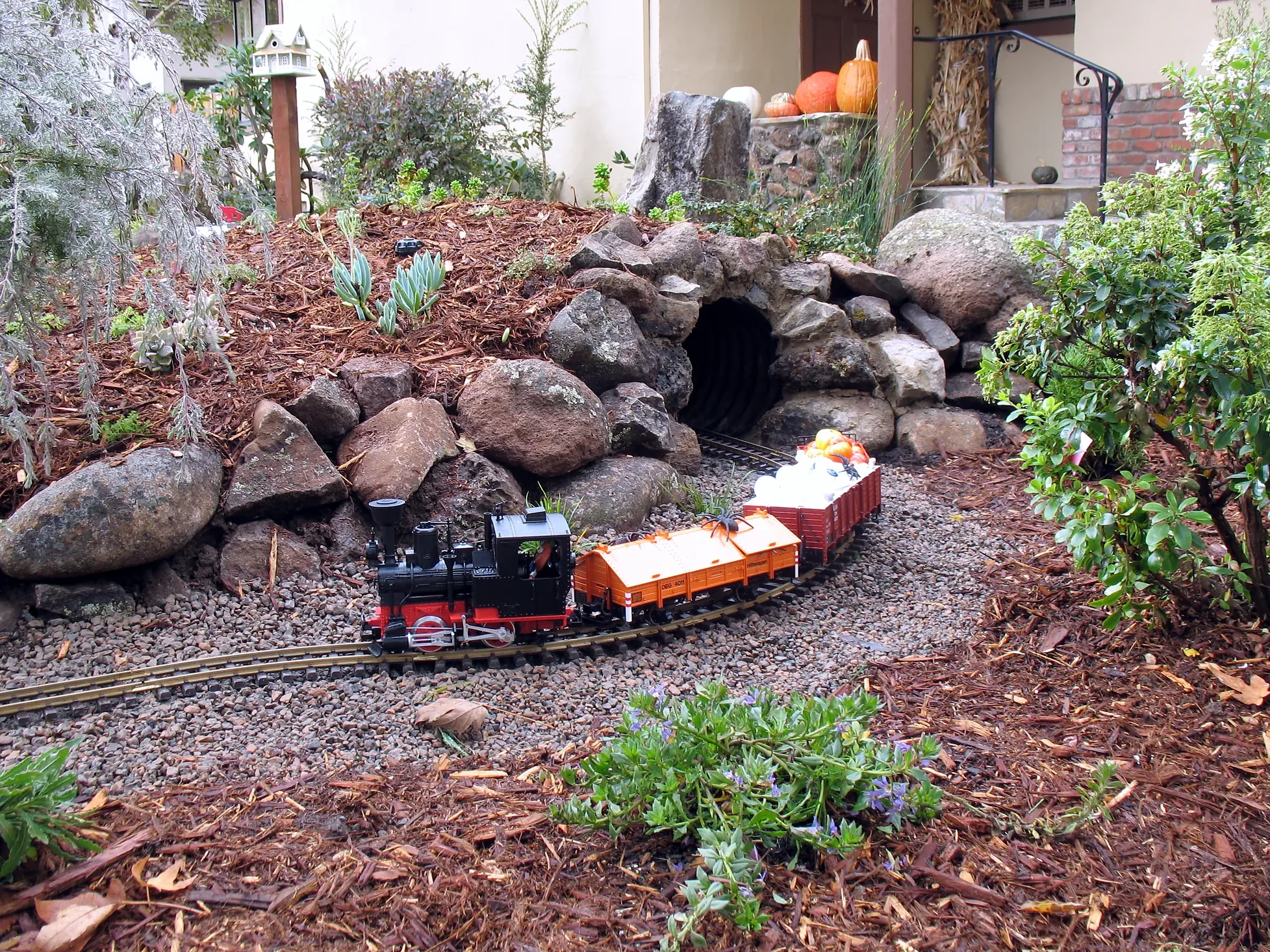 Los Altos family garden — the front garden railway, a steam engine and cars passing a stone tunnel, with the front porch behind