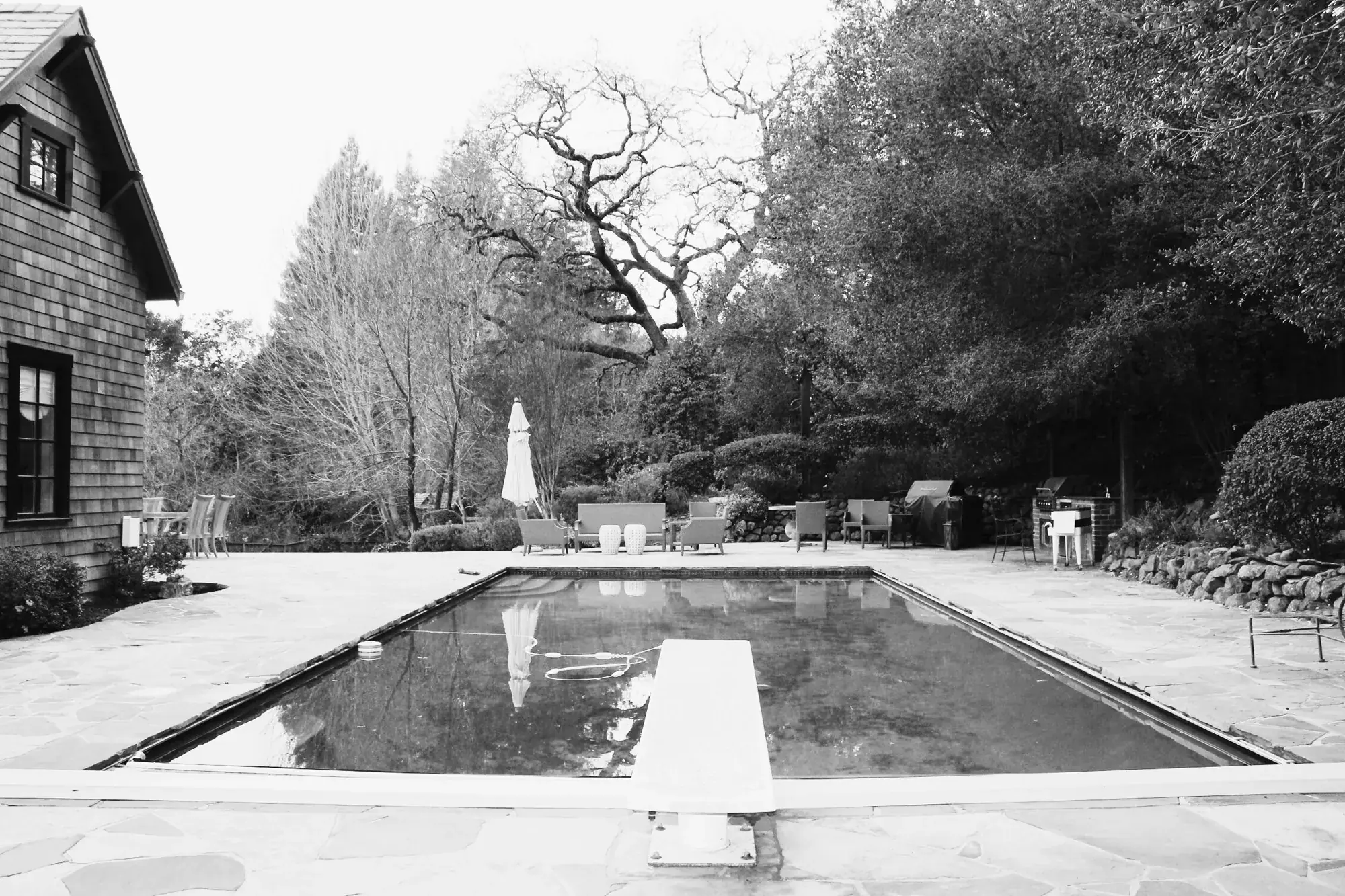 Before — the original pool with its diving board, ringed by flagstone paving and a dry-stacked rock wall