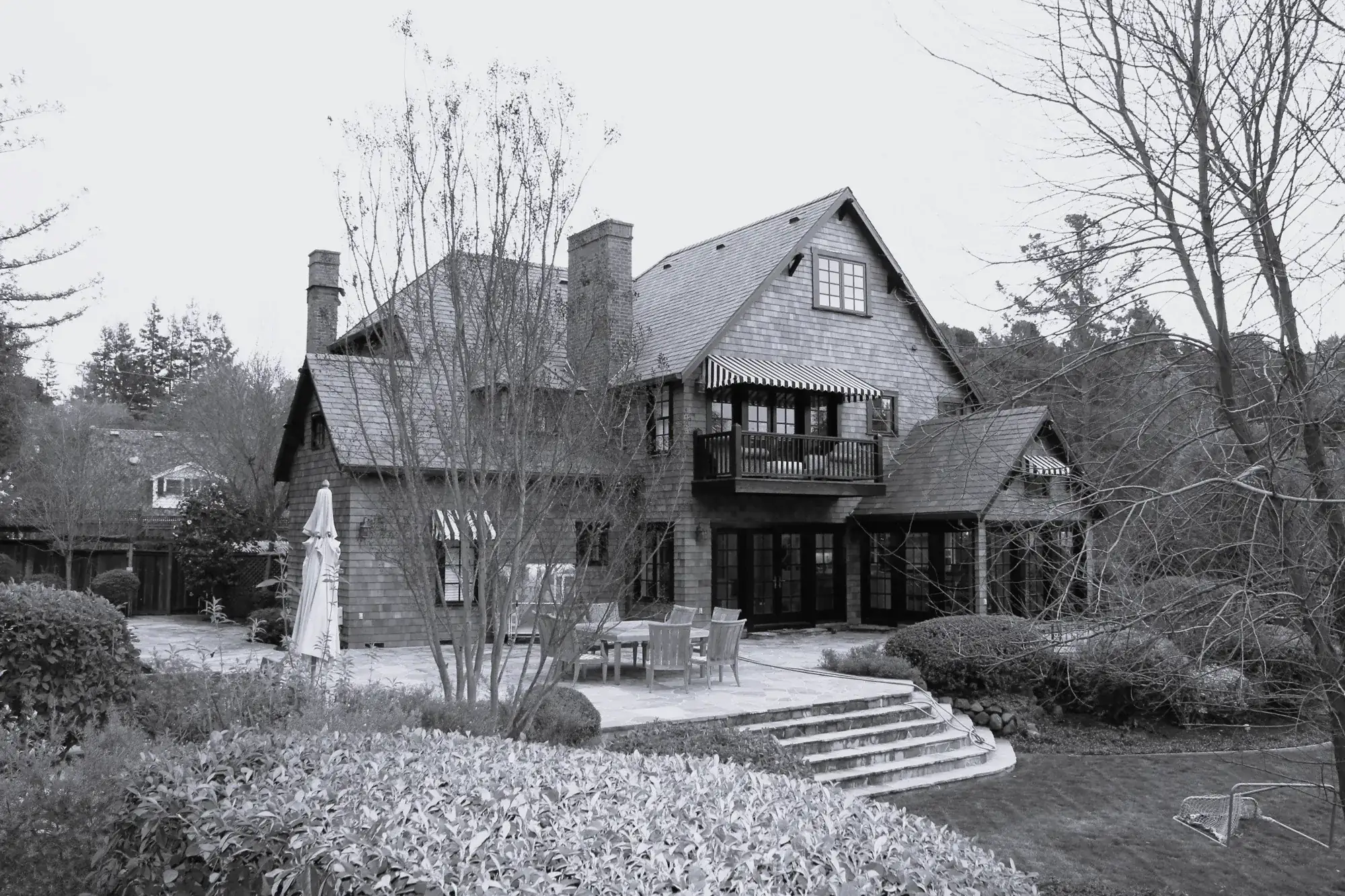 Before — the rear of the shingled house, with a table and chairs on a narrow patio under retractable awnings