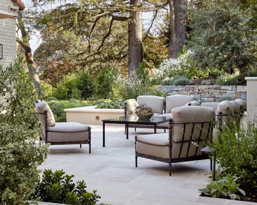 The stone sitting terrace — iron lounge chairs around a low table, backed by a dry-stacked stone wall under the cedars