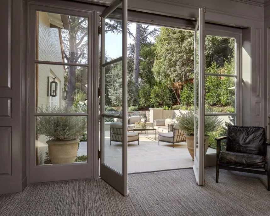 The garden seen through open French doors — potted rosemary flanking the step down to the stone patio and its sitting area