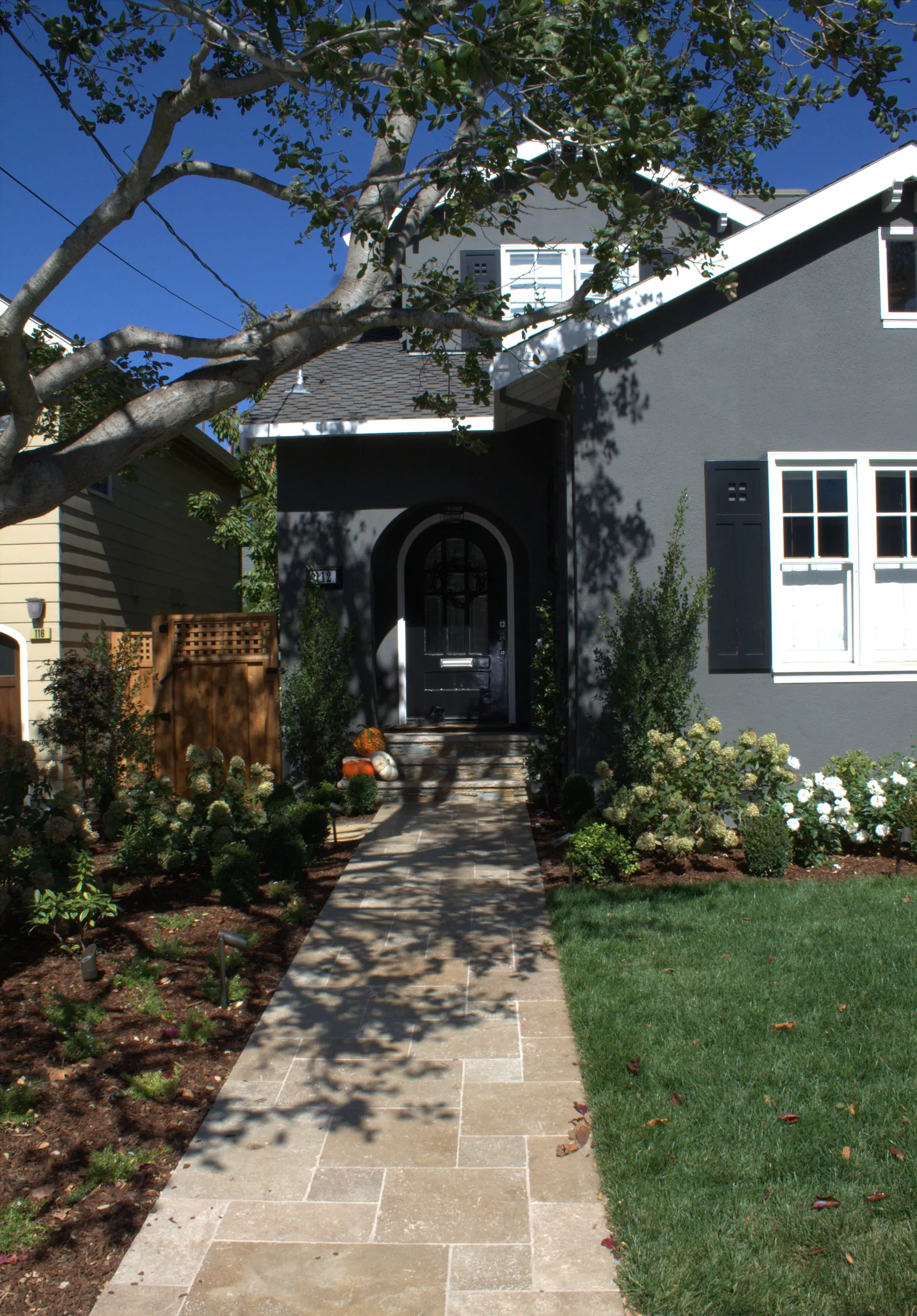 After photo — the same entry, with a travertine walk approaching the arched front door, hydrangeas and white roses to either side