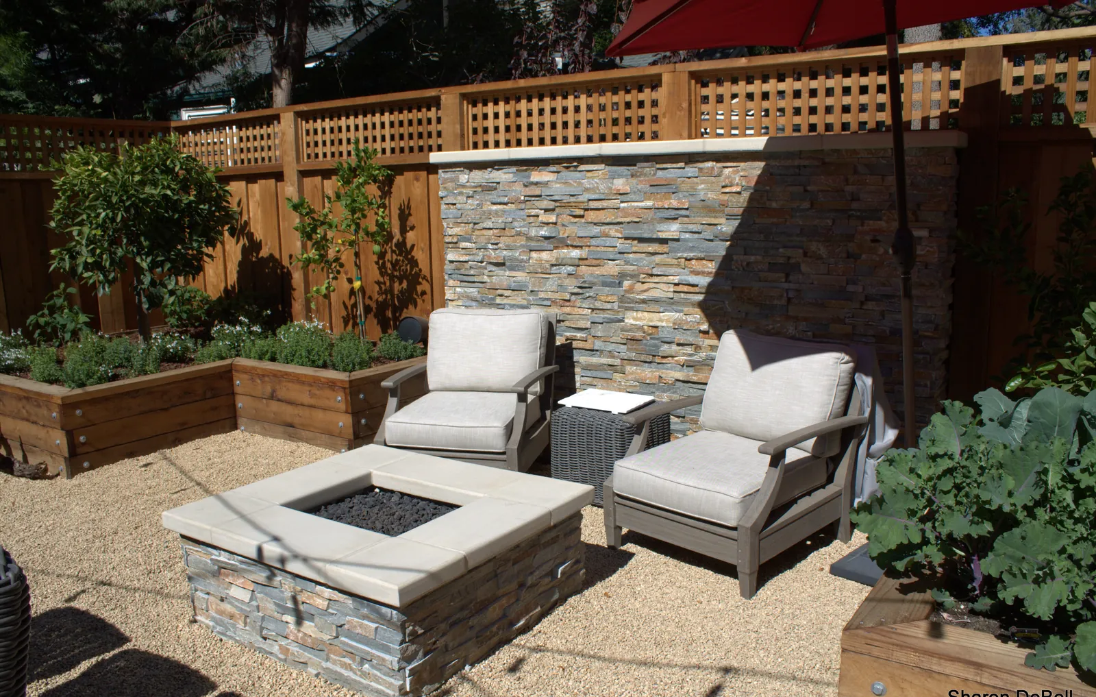 The fire-pit corner — two lounge chairs against the stacked-stone privacy wall, with espaliered lemons and raised herb beds behind