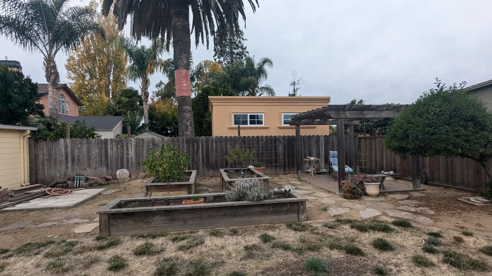 Before photo — the original raised planter beds, weathered and worn, with patchy lawn and the existing pergola beyond