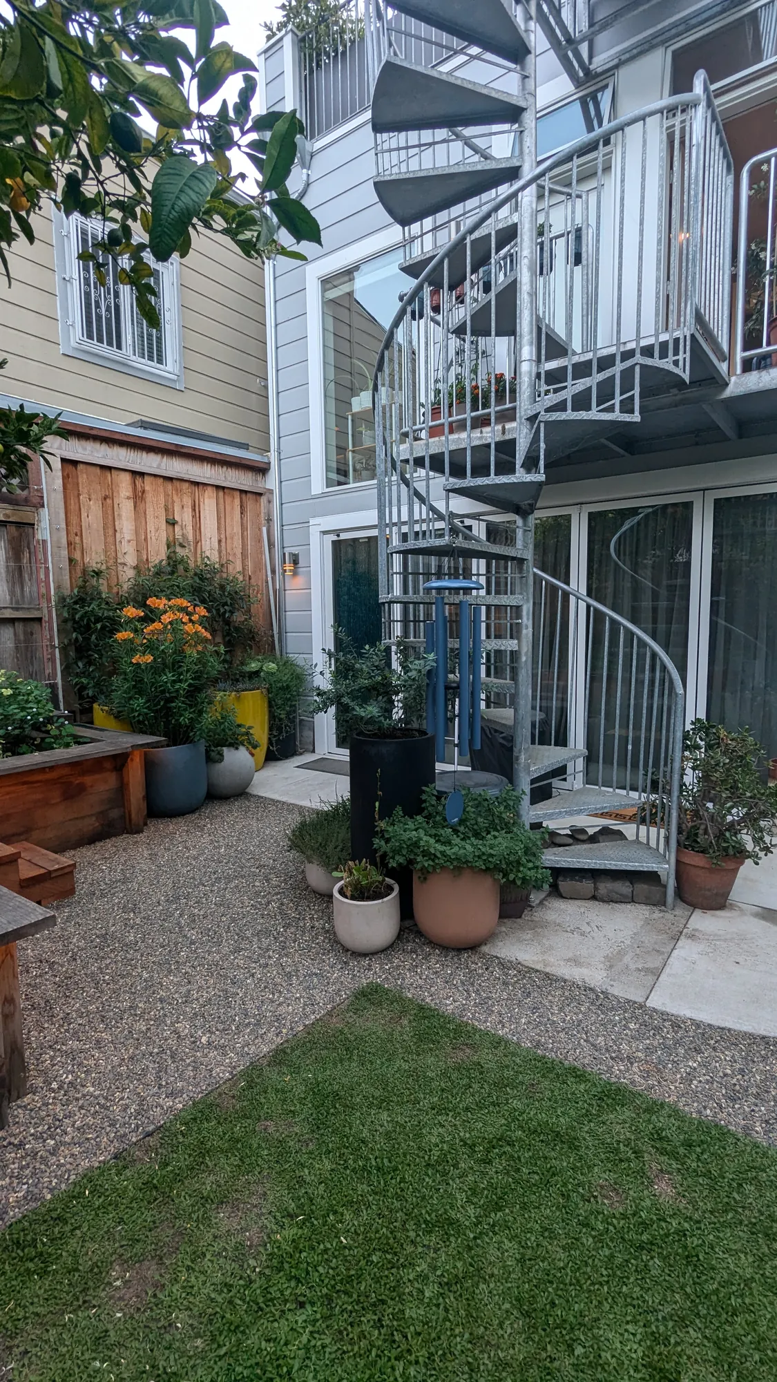 The spiral stair linking the levels — rising from the backyard gravel and lawn past the mid-level deck to the roof garden above