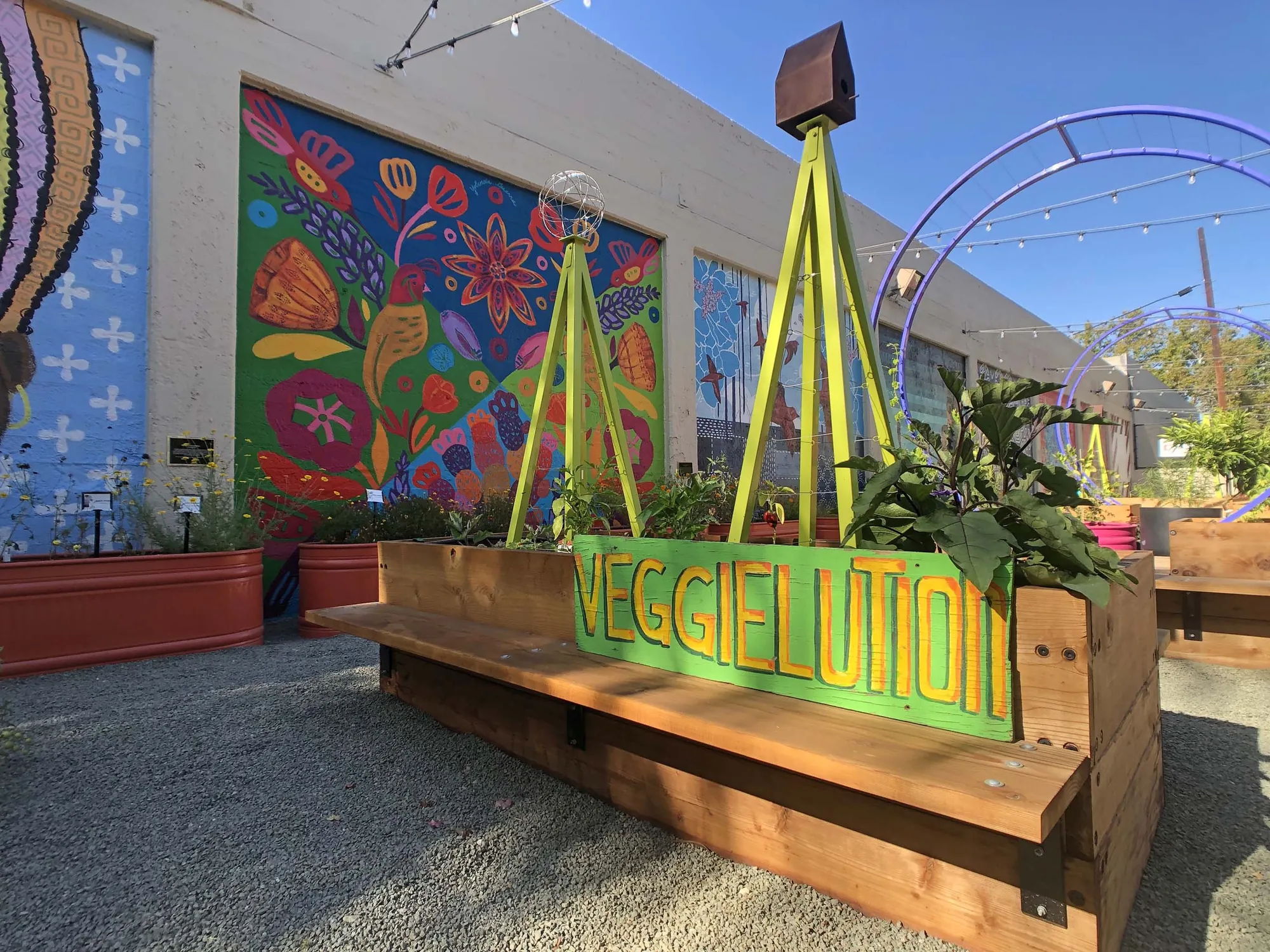 SoFA Pocket Park, San Jose — a bench planter with chartreuse A-frame trellises, red stock-tank planters, and floral murals