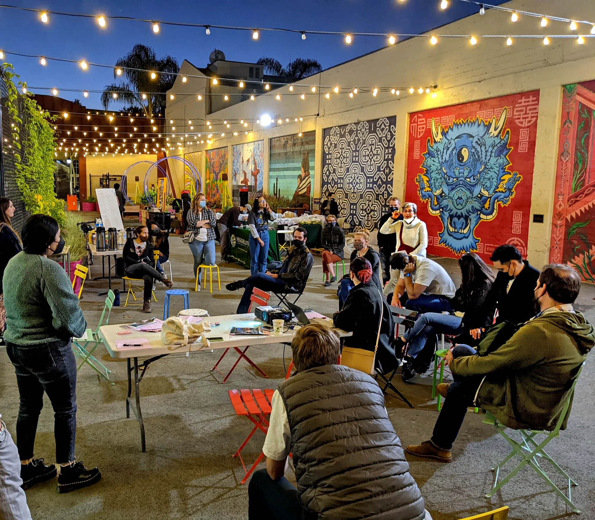 SoFA Pocket Park at dusk — a community gathering under string lights, framed by murals