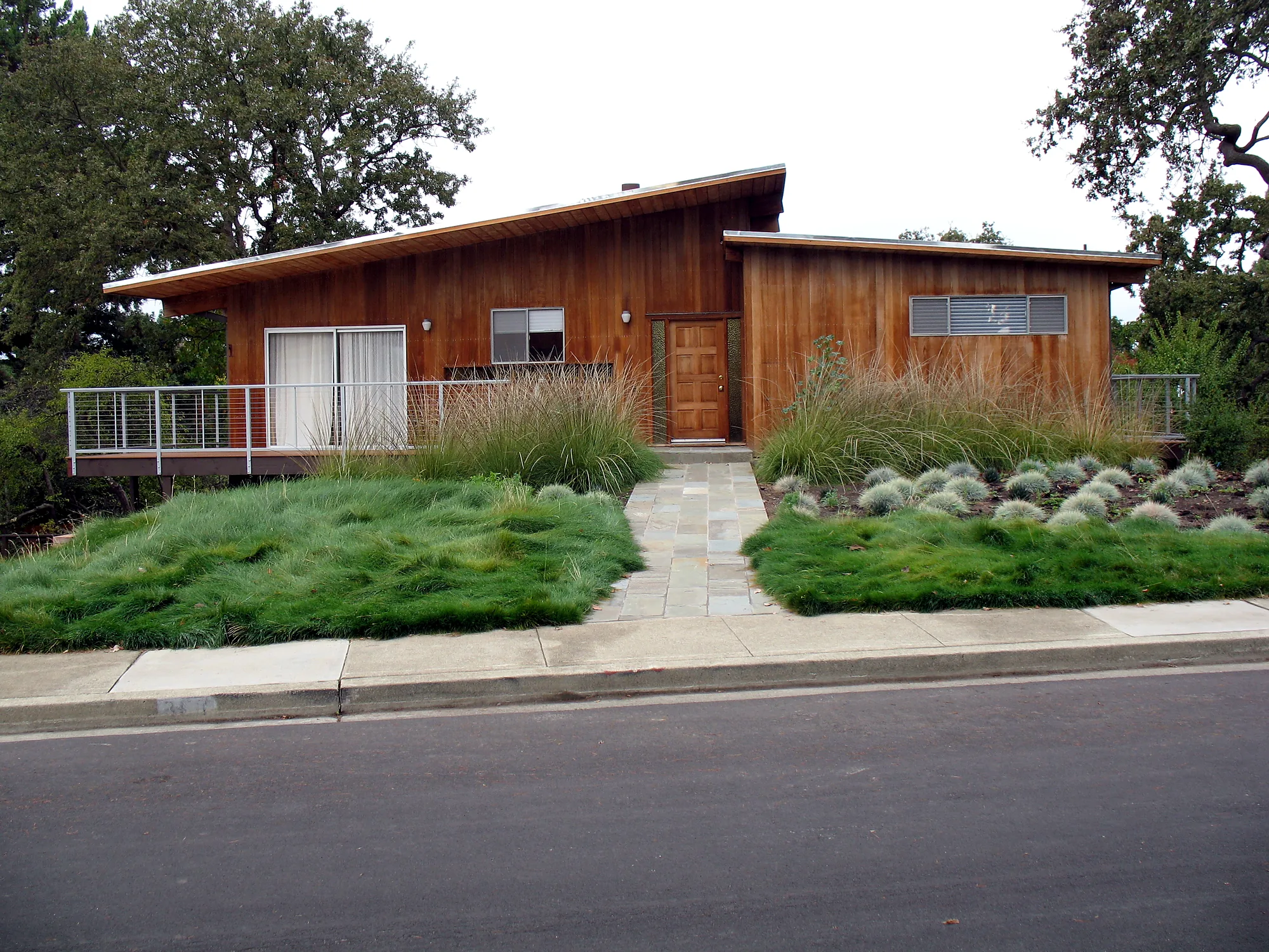 Stanford Residence — the mid-century wood house seen from the street behind a no-mow fescue meadow, deer grass, and a full-range bluestone entry walk