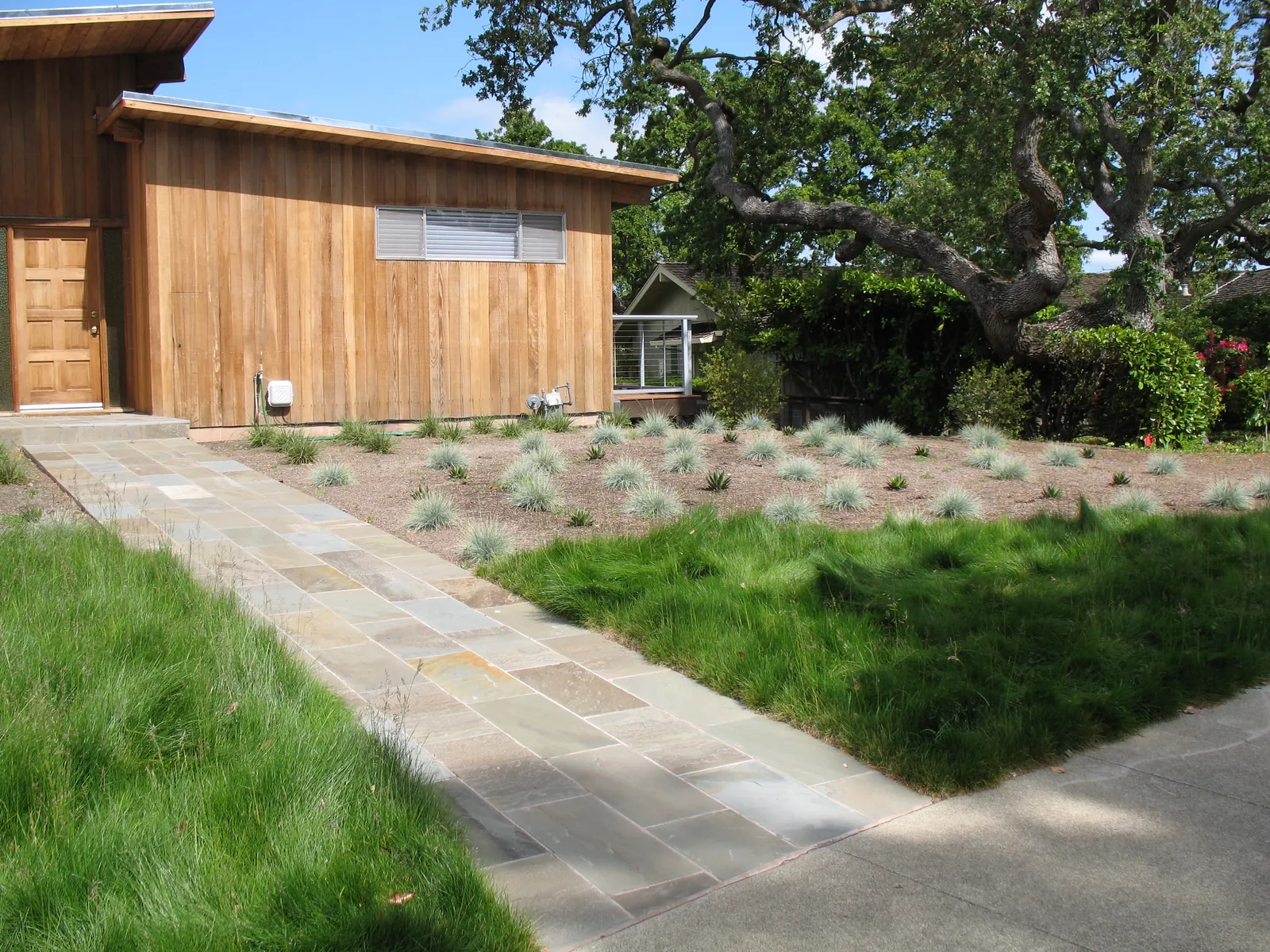 A full-range bluestone walk cutting between the meadow and newly mulched beds, the wood house behind