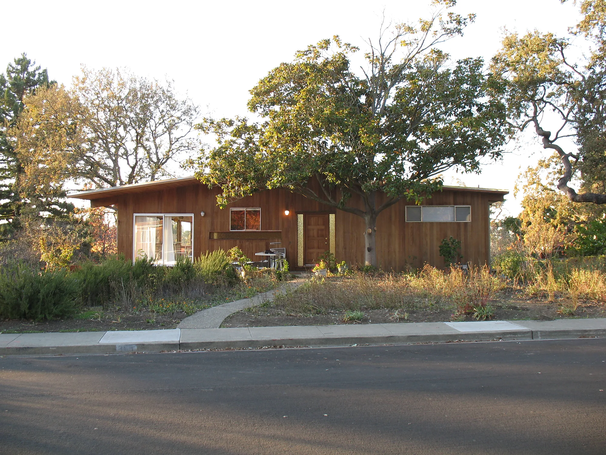 Before — the same house from across the street in 2011, bare dirt and dry weeds between the sidewalk and the deck
