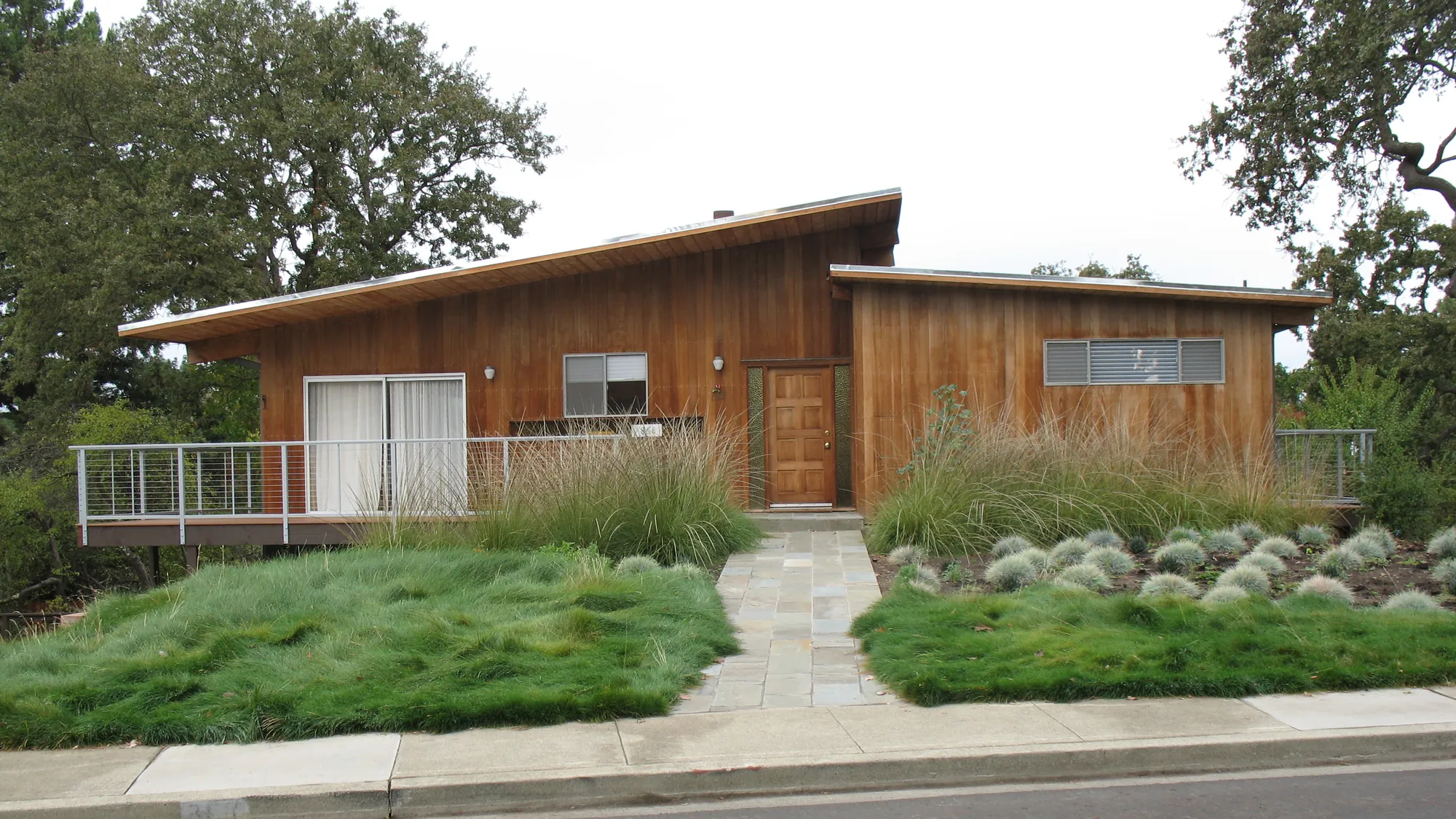 Stanford Residence — the mid-century wood house seen from the street behind a no-mow fescue meadow, deer grass, and a full-range bluestone entry walk